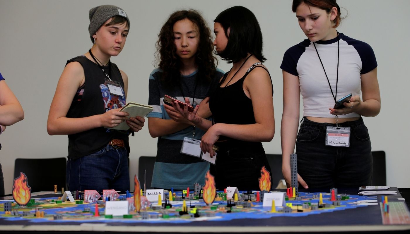 Vier Jugendliche stehen an einem großen Spielbrett und arbeiten konzentriert am Weltklimaspiel.